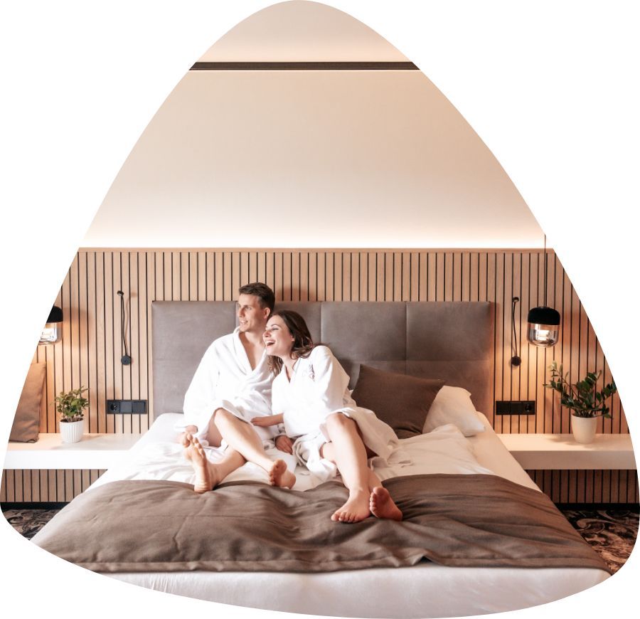 Pärchen im Bademantel liegt im Bett und blickt aus dem Fenster.